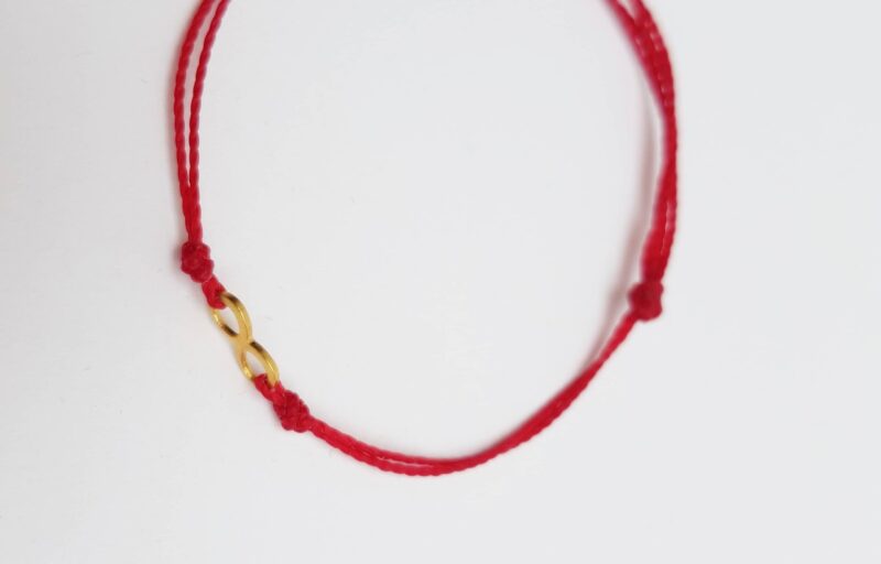 Bransoletka z czerwonego sznurka z łącznikiem w kształcie znaku nieskończoności.