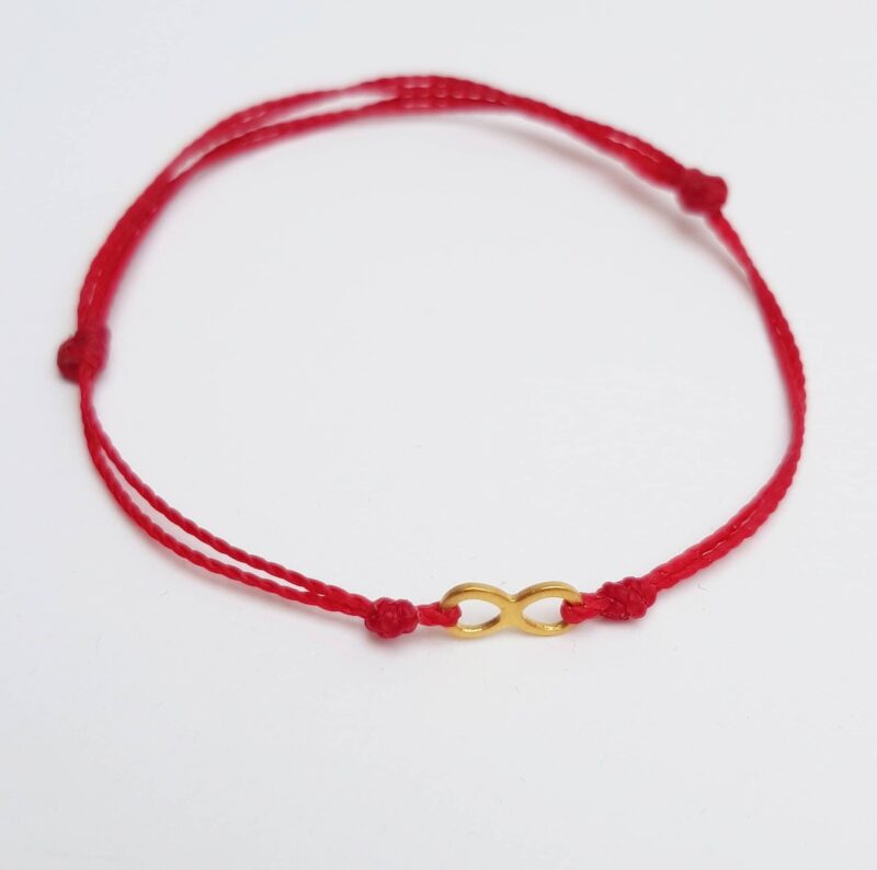 Bransoletka z czerwonego sznurka z łącznikiem ze stali szlachetnej w kolorze złotym, w kształcie znaku nieskończoności.