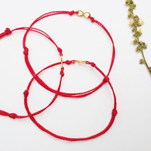 Bransoletka z czerwonego sznurka z łącznikiem ze stali szlachetnej w kolorze złotym, w kształcie znaku nieskończoności.