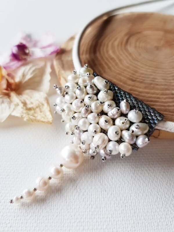 Naszyjnik Perlisty w formie zawieszki, powstał z różnej wielkości pereł hodowlanych w białym kolorze i szarych koralików szklanych, zawieszony na skórzanym rzemyku.