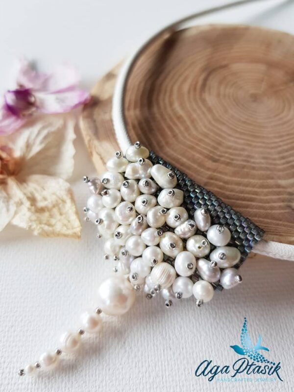 Naszyjnik Perlisty w formie zawieszki, powstał z różnej wielkości pereł hodowlanych w białym kolorze i szarych koralików szklanych, zawieszony na skórzanym rzemyku.