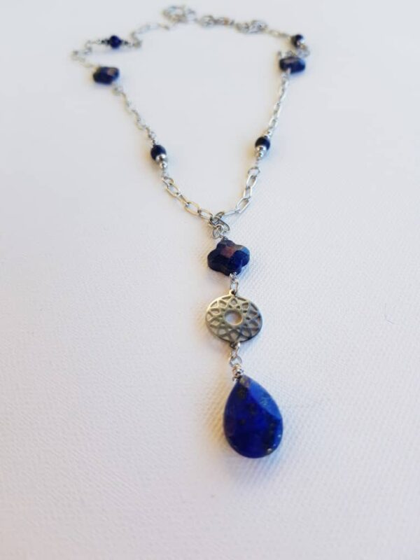 Długi naszyjnik srebrny Posłaniec Niebios z lapis lazuli to urocza kompozycja różnych kształtów niebieskiego minerału- koniczynki, kulki, kropla, hematytów oraz łańcuszka typu spinacz i mandali ze stali szlachetnej.