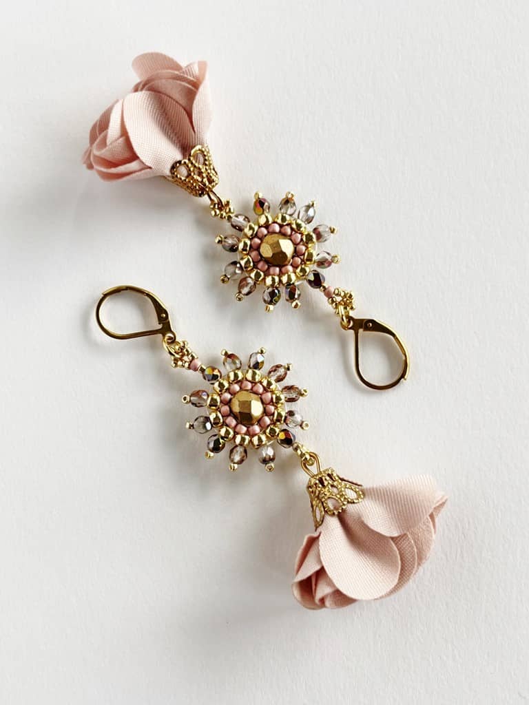 Kolczyki Wiosenne Kwiaty pudrowy róż zostały wyplecione z różowych i złotych koralików szklanych z dodatkiem delikatnych różowych tekstylnych zawieszek w kształcie kwiatów.