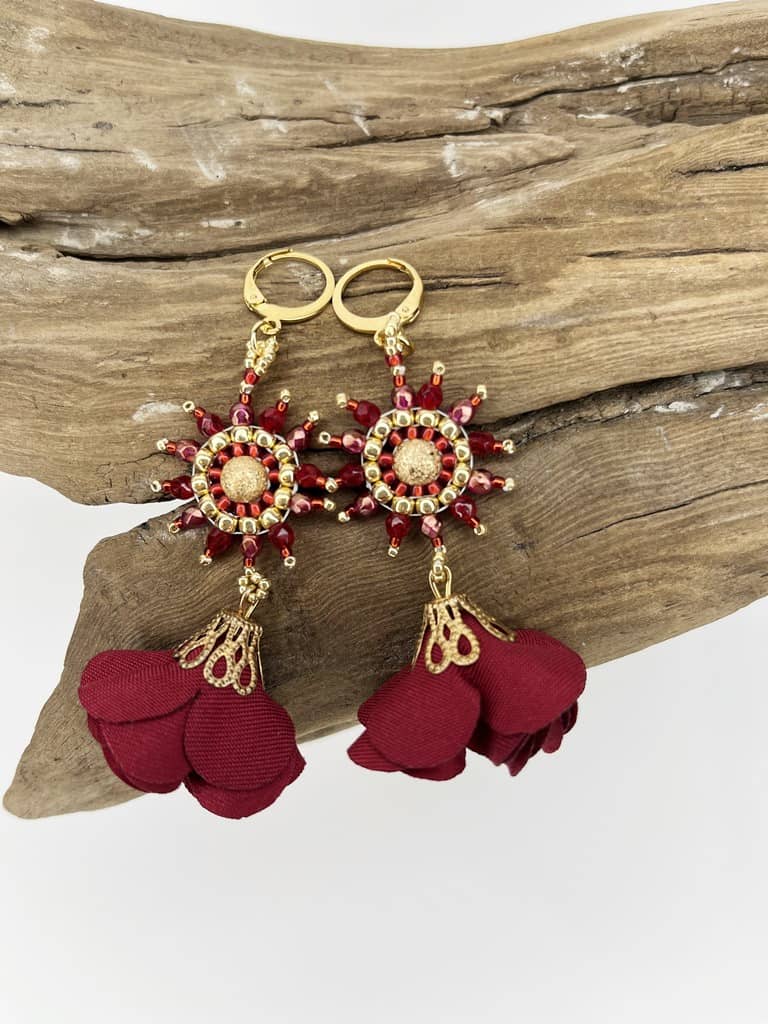 Kolczyki Wiosenne Kwiaty Bordowe zostały wyplecione z czerwonych i złotych koralików szklanych z dodatkiem delikatnych bordowych tekstylnych zawieszek w kształcie kwiatów.