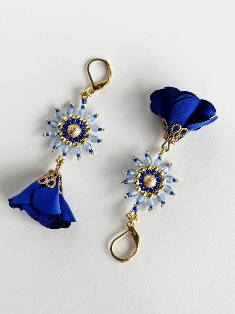 Kolczyki Wiosenne Kwiaty Kobalt zostały wyplecione z kobaltowych, błękitnych i złotych koralików szklanych z dodatkiem delikatnych kobaltowych tekstylnych zawieszek w kształcie kwiatów.