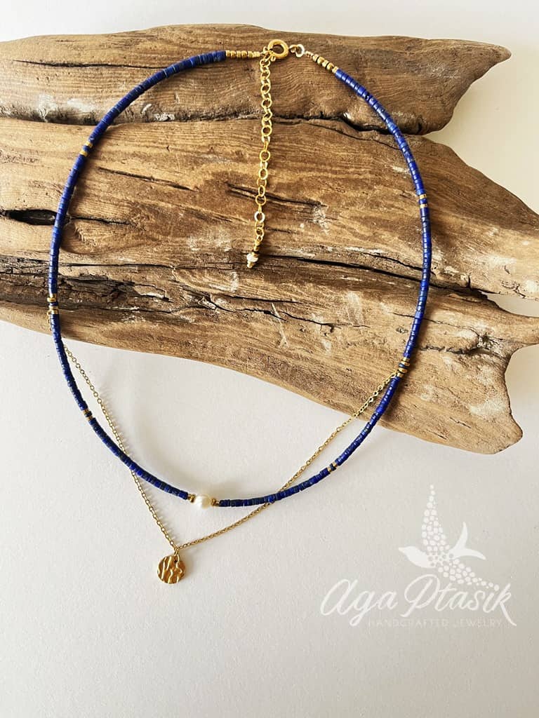 Naszyjnik układający się warstwowo wykonany z kamieni lapis lazuli, i perły oraz łańcuszka z okrągłą zawieszką.